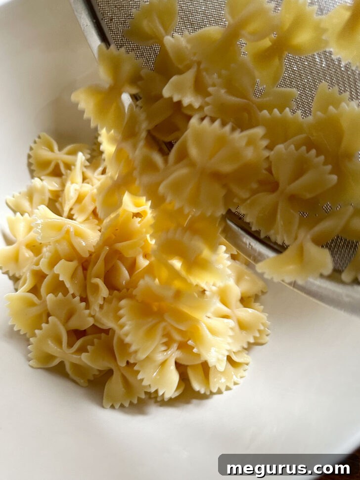 Cooked and thoroughly drained bowtie pasta being added to a large, empty salad bowl, ready for the remaining ingredients.