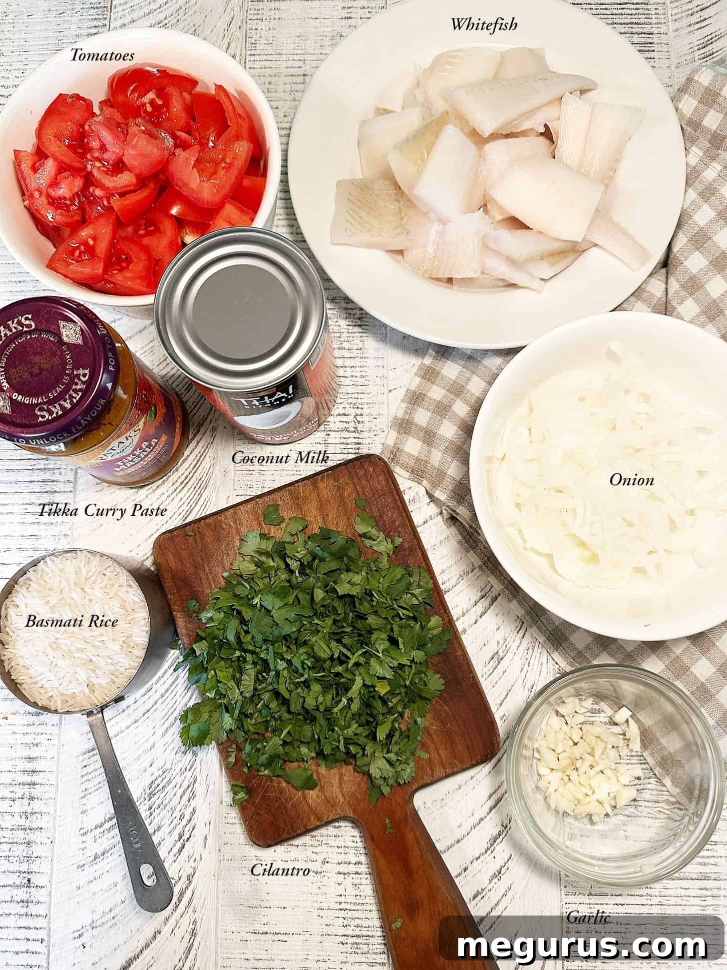 Close-up shot of the fresh ingredients for coconut fish curry, including whitefish, tomatoes, coconut milk, and curry paste.