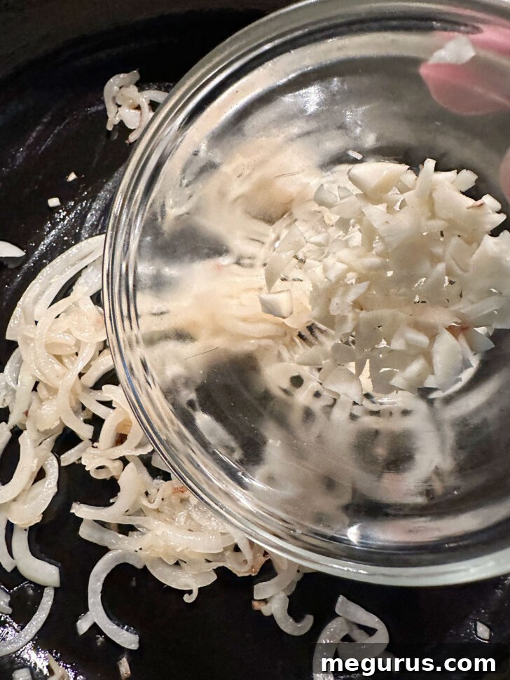 Adding chopped garlic to a skillet with sautéing onions.