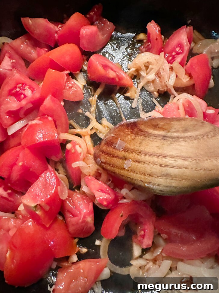 Freshly chopped tomatoes being added to the skillet with onions and garlic.