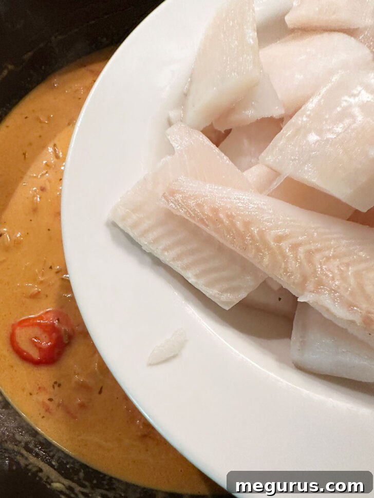 Pieces of whitefish being carefully placed into the simmering coconut curry sauce.