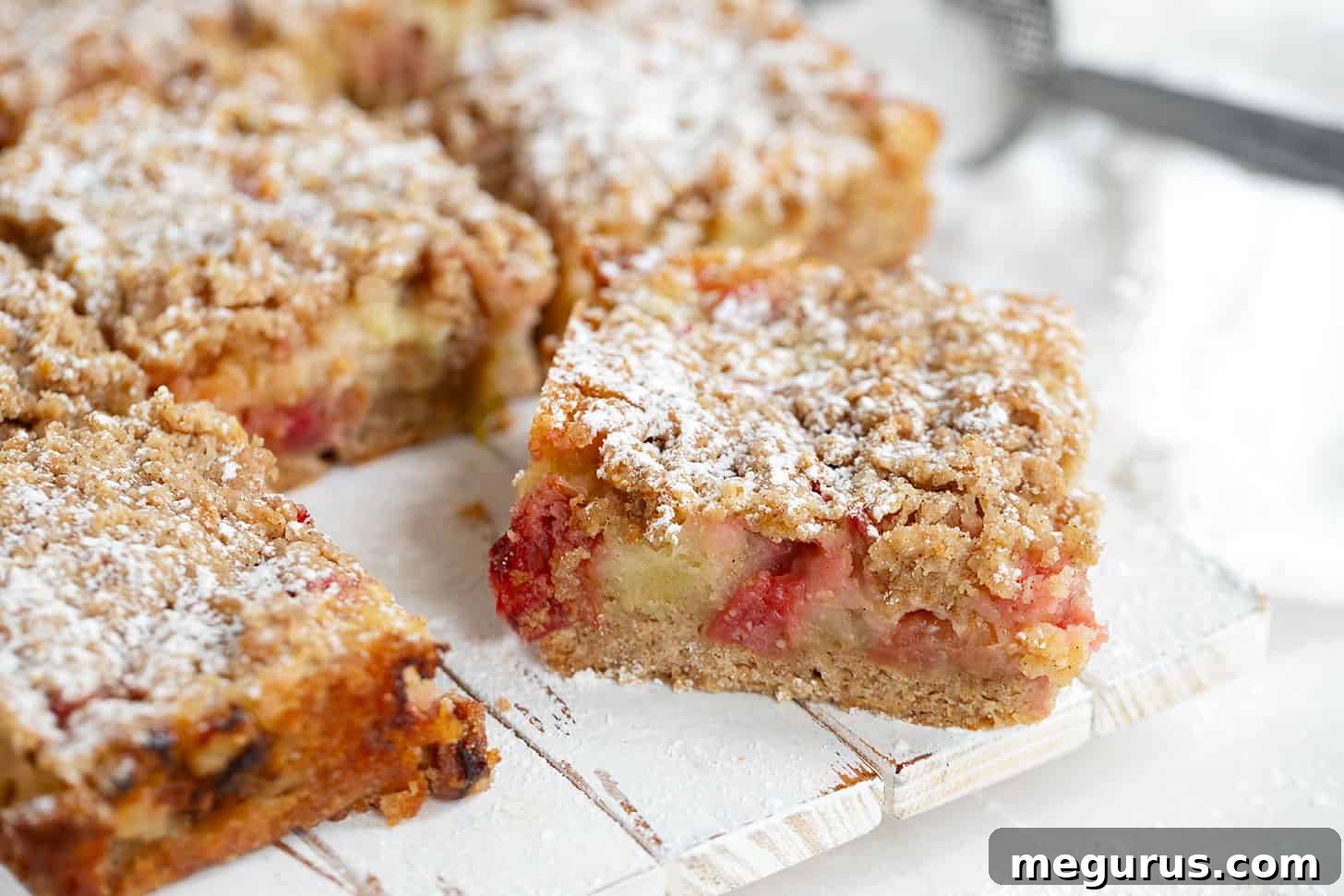 A slice of homemade rhubarb custard cake on a wooden serving board, showcasing its distinct layers.