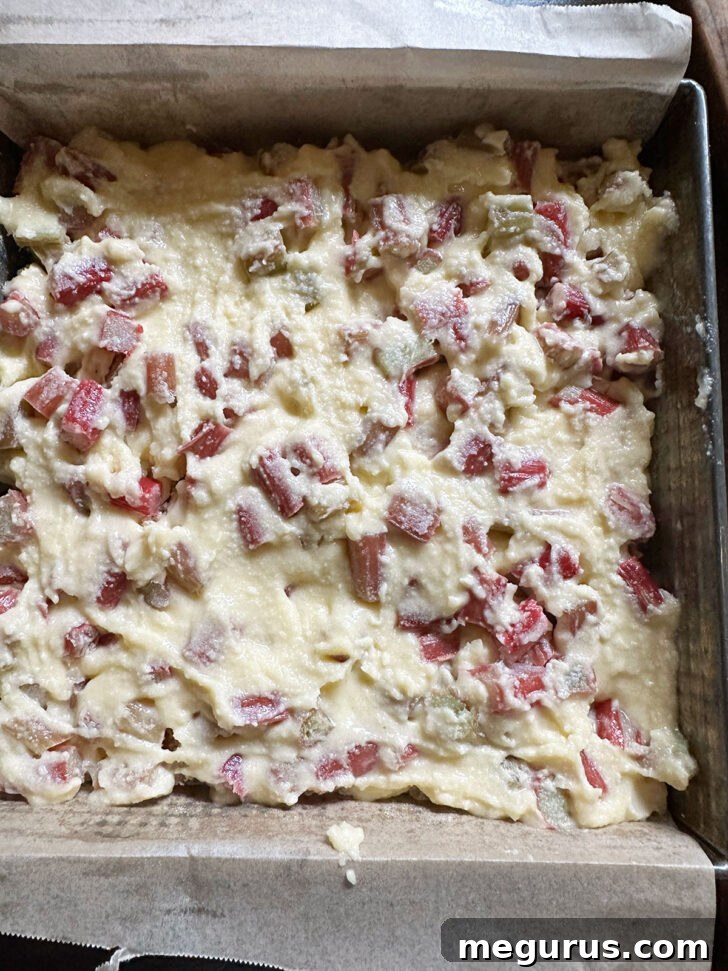 The rhubarb custard filling being spread evenly over the crumb base in the baking pan.