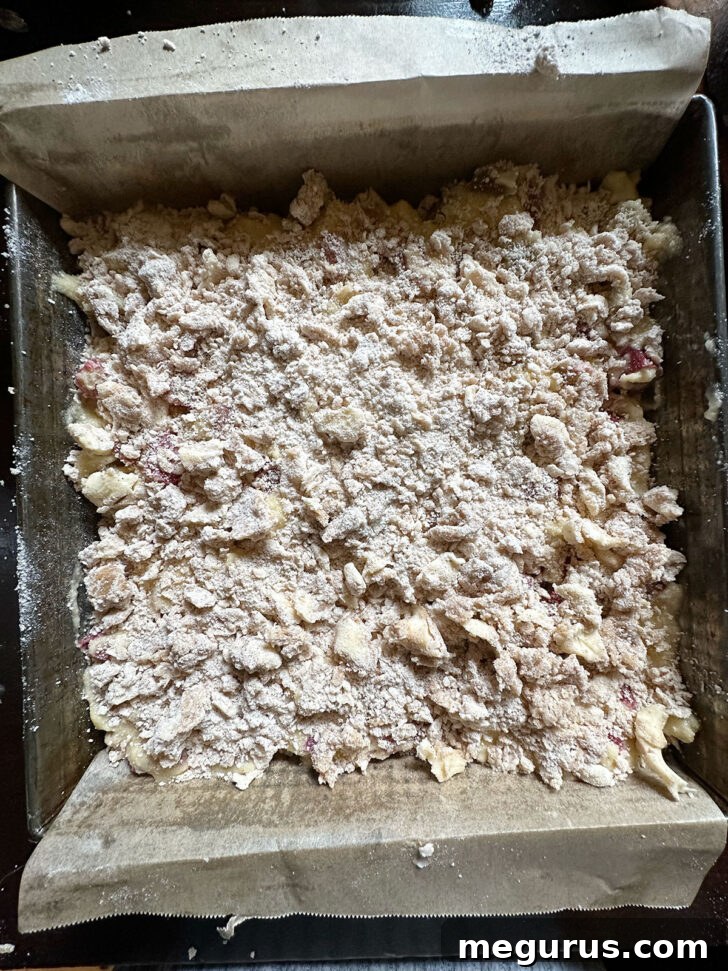 The reserved crumb mixture being spooned over the top of the rhubarb custard cake before baking.