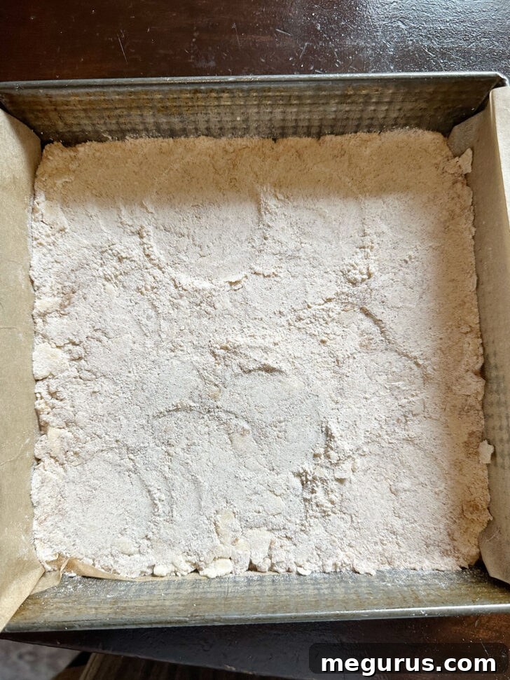 The crumb mixture being firmly pressed into the bottom of the baking pan to form the base.