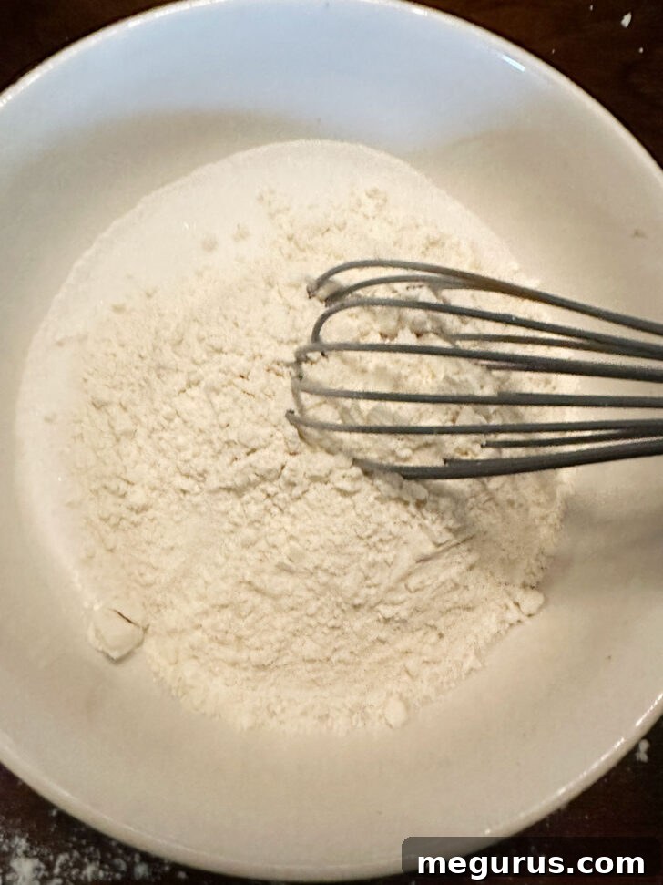 Dry ingredients for the custard filling (sugar and flour) being whisked together in a large bowl.