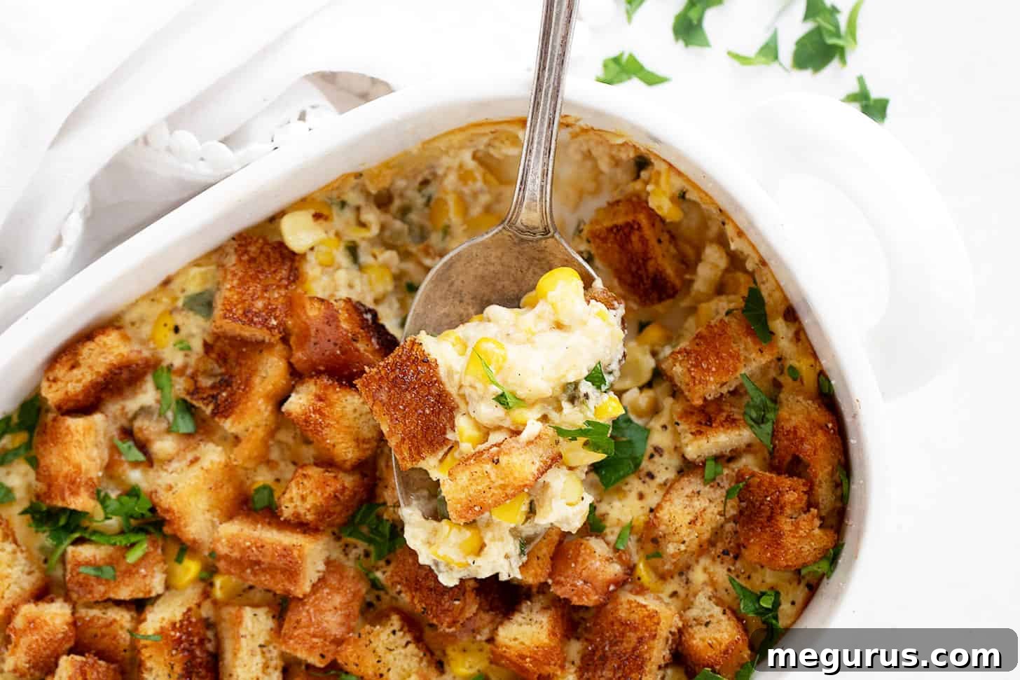 Golden-brown scalloped corn casserole in a baking dish, served with a spoon.