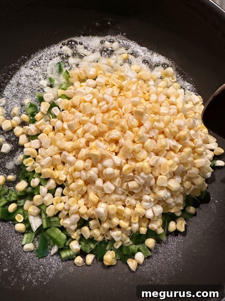 Diced onion, jalapeño, and fresh corn kernels sautéing in a skillet with butter.