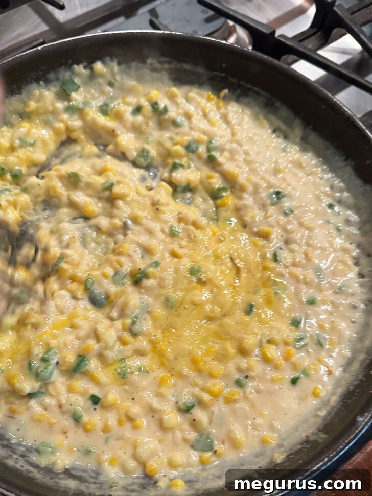 A whisk stirring a slightly beaten egg into the corn and white sauce mixture in a skillet.