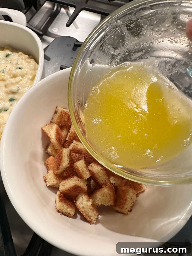 Melted butter being poured over cubed bread croutons in a bowl.