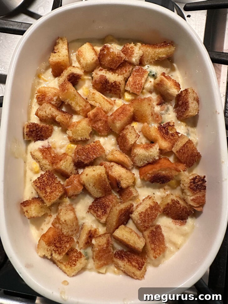 Unbaked scalloped corn casserole topped with croutons in a baking dish, ready for the oven.