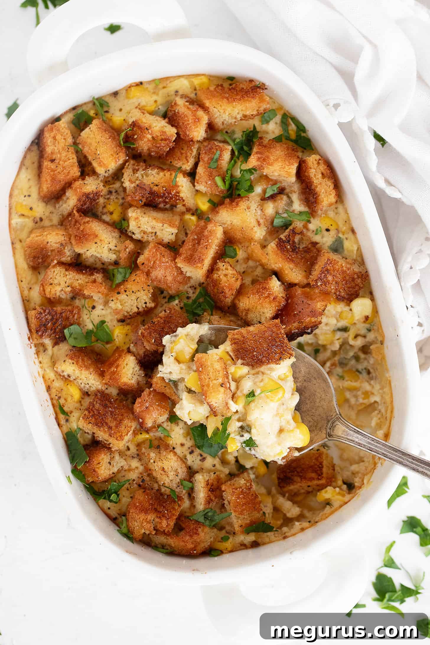 Scalloped corn casserole in baking dish with a spoon, highlighting its creamy texture and crispy topping.