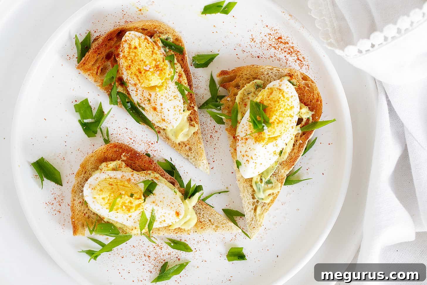 Open-faced devilled egg sandwiches on a serving plate, garnished with paprika and fresh herbs.