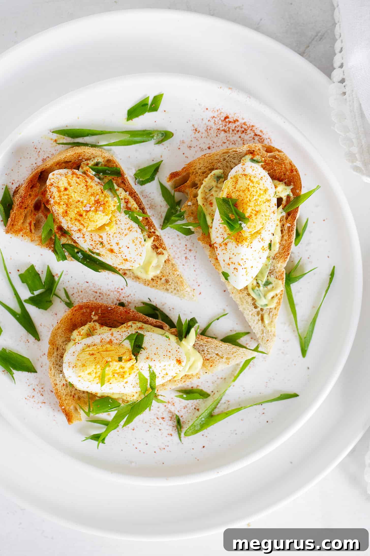 Beautifully plated open-faced devilled egg sandwiches, garnished with paprika and herbs.