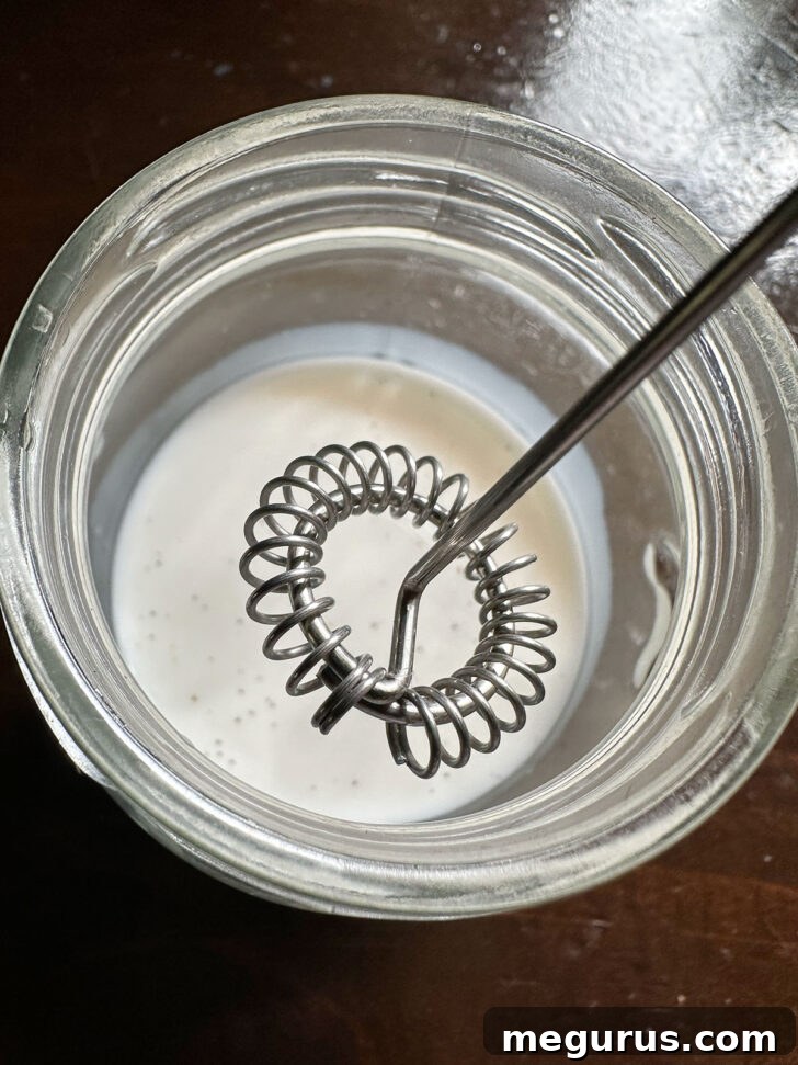 Half and half cream and vanilla simple syrup being frothed together using a handheld frother in a small glass jar.