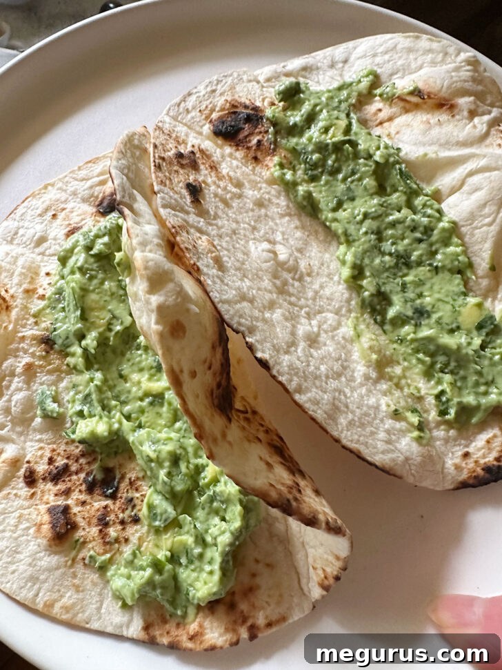 Avocado sauce generously spread onto a warm tortilla, ready for the filling.