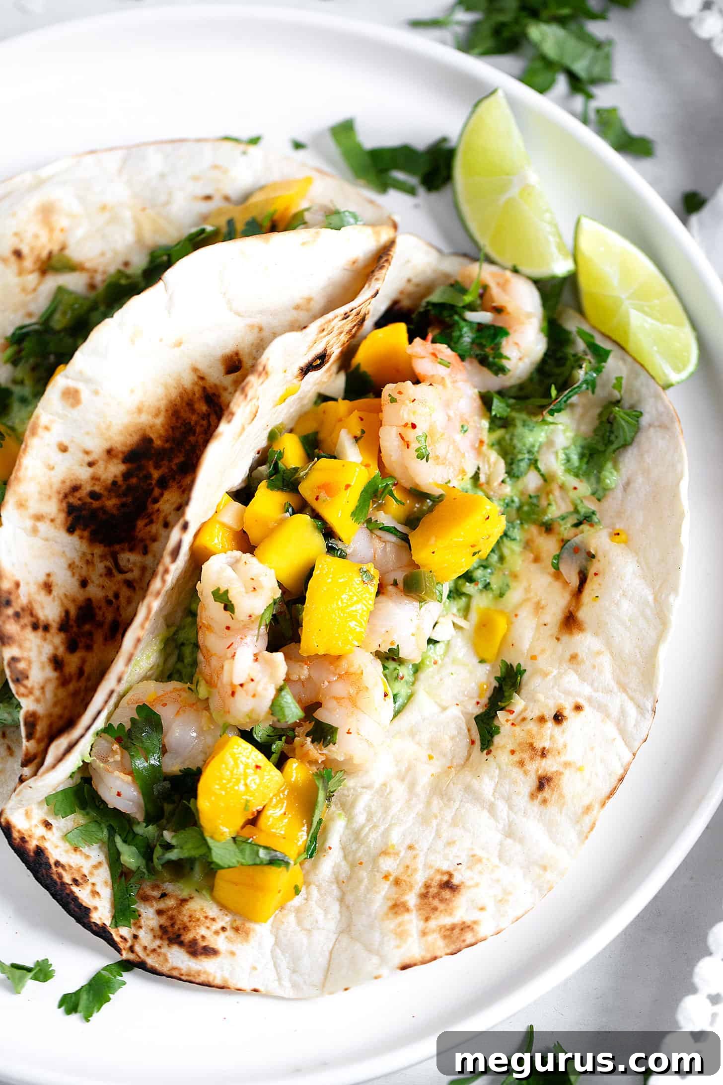 A vibrant close-up of fully assembled mango shrimp tacos, showcasing the colorful filling and creamy sauce.