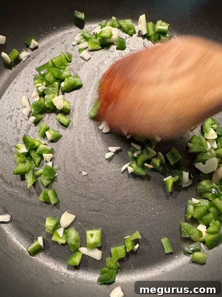 Sautéing diced jalapeño and minced garlic in a hot skillet, releasing aromatic flavors.