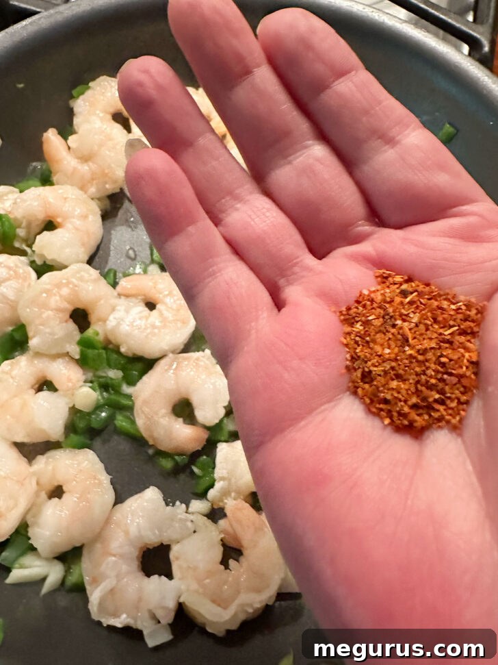 Sprinkling vibrant Tajín seasoning over the shrimp mixture in the skillet.