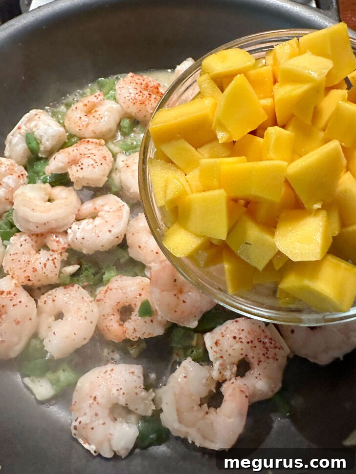 Incorporating sweet, diced mango into the skillet with the cooked shrimp and spices.