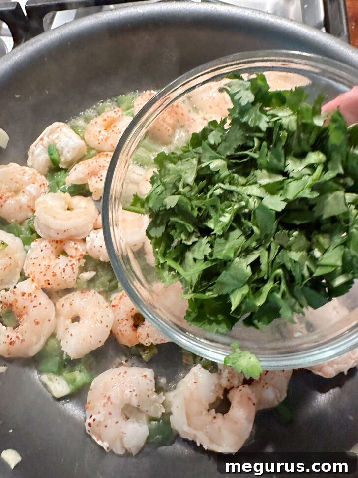 Fresh cilantro being added to the shrimp and mango mixture in the skillet.