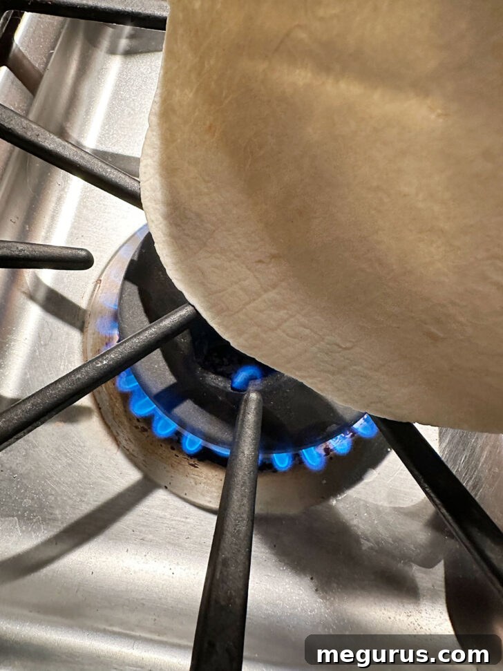 Heating tortillas directly over a gas stove flame for a slight char and warmth.