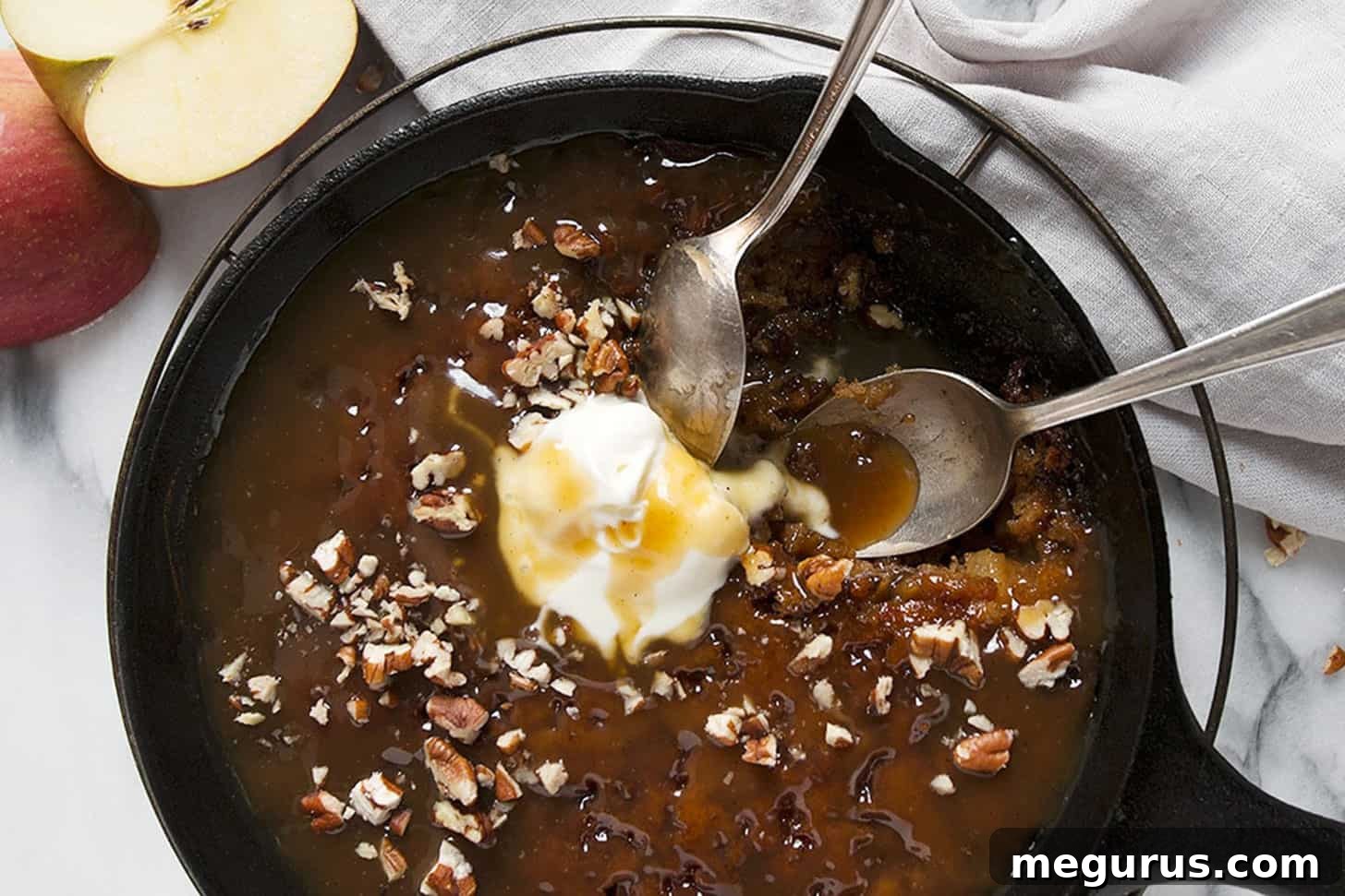 Warm Apple Sticky Toffee Pudding served in a cast iron skillet, topped with a scoop of melting vanilla ice cream.