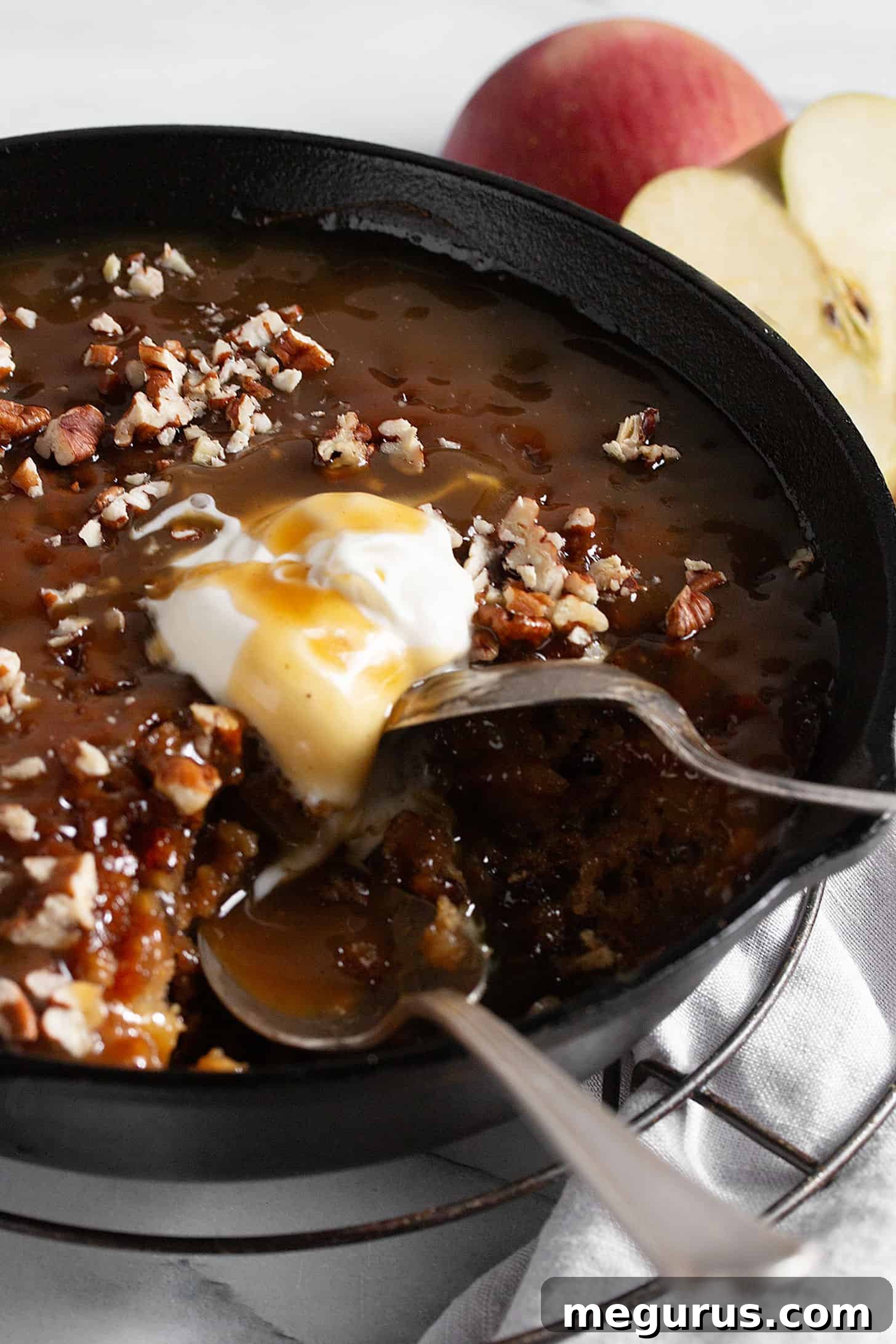 Apple sticky toffee pudding in a cast iron skillet with a generous helping of toffee sauce and a scoop of vanilla ice cream.