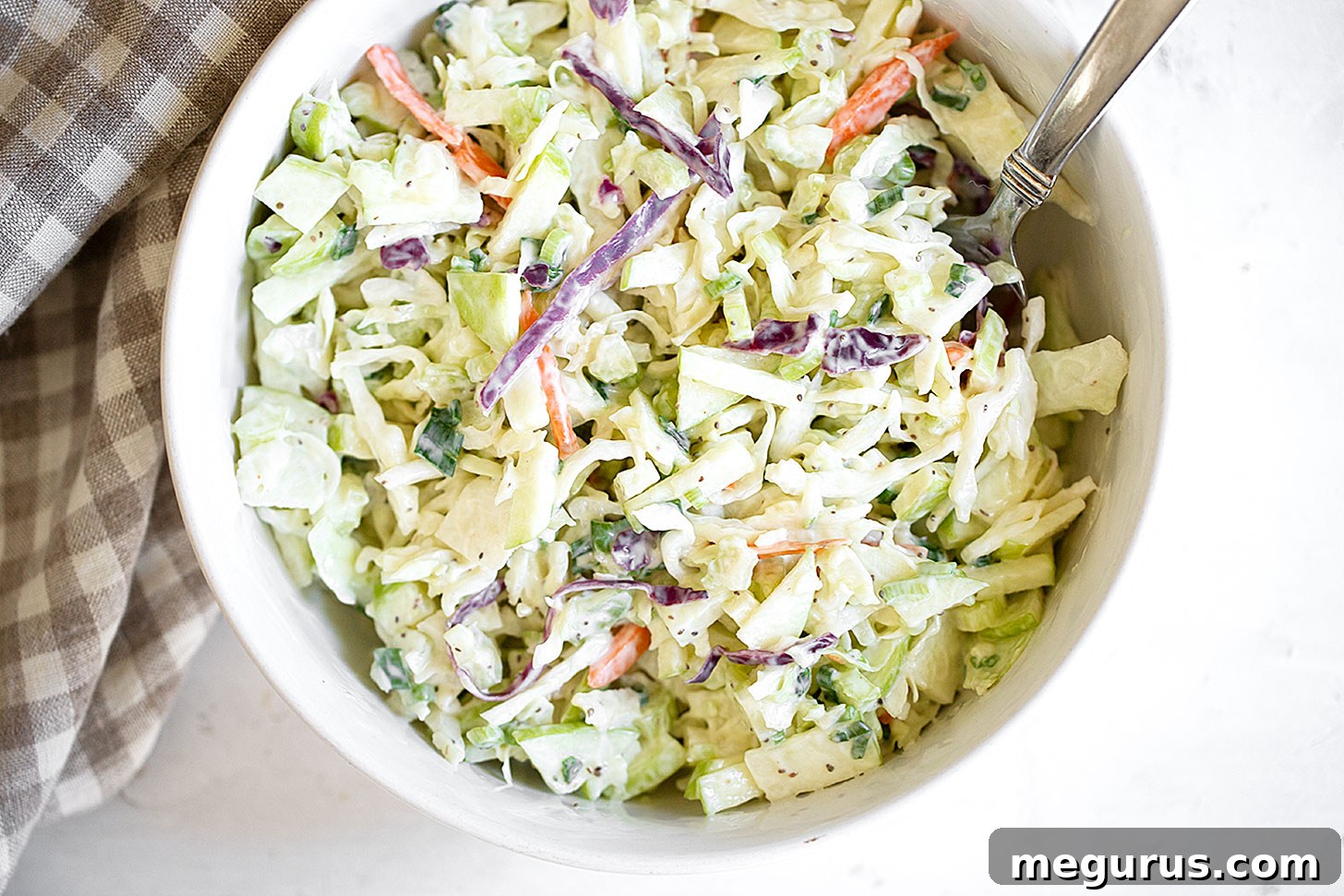 A generous bowl of creamy coleslaw, perfectly dressed and ready to serve, with a spoon resting in it.