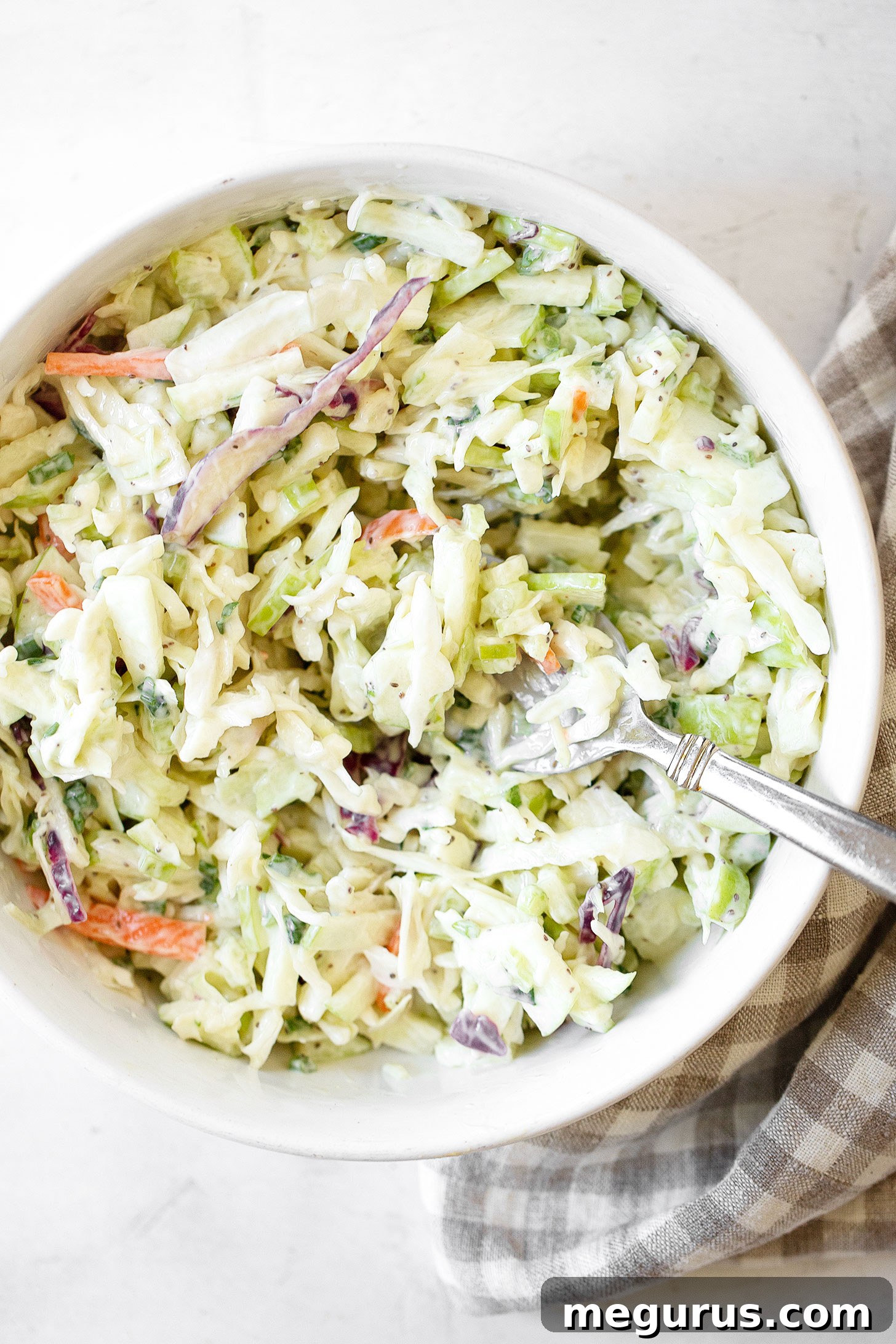 A close-up of creamy coleslaw in a bowl, with a serving spoon highlighting its rich texture and the crispness of the shredded vegetables.