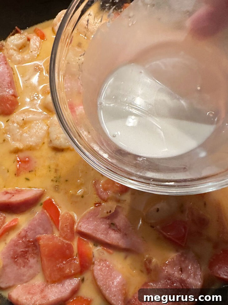 Cornstarch and water slurry being drizzled into the simmering Cajun sauce to thicken it.