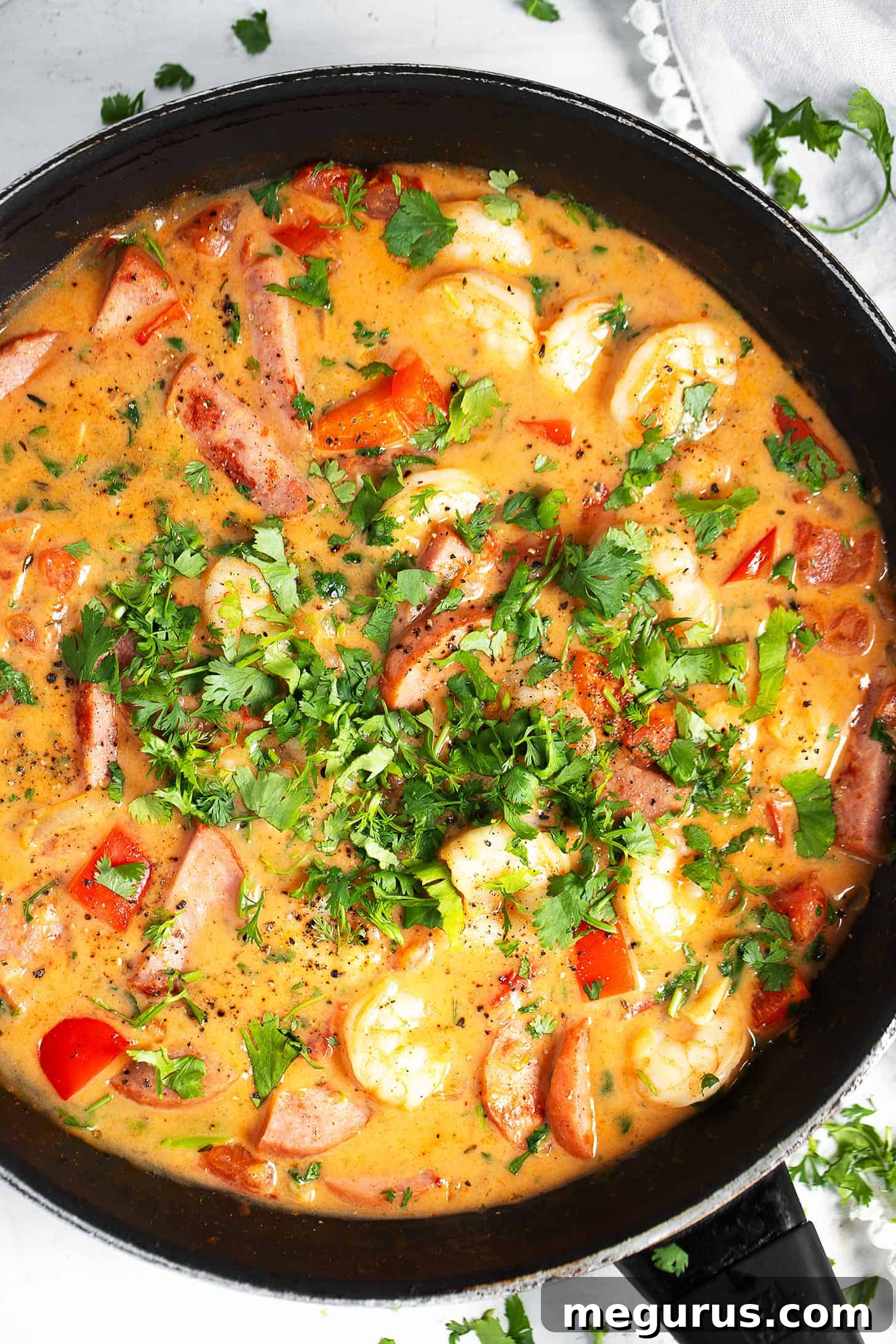 A generous serving of Cajun shrimp and sausage in a skillet, close-up, showcasing the rich sauce and fresh herbs.