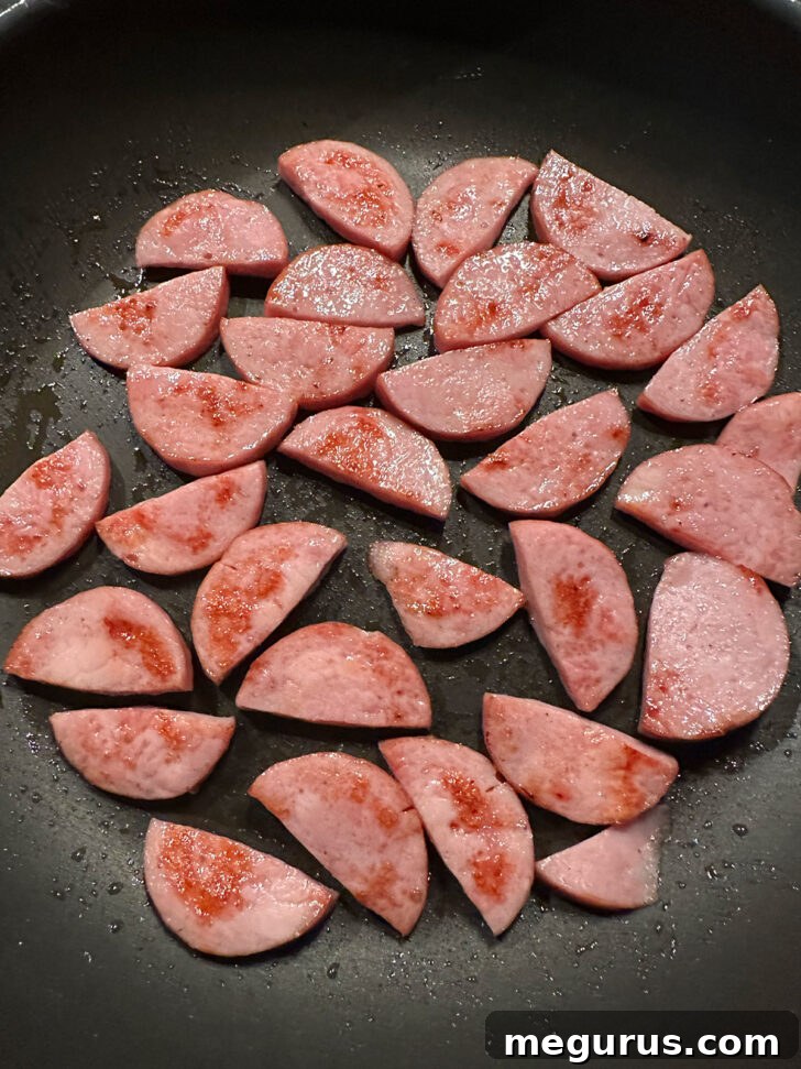 Slices of Kielbasa sausage browning in a hot skillet, developing a golden crust.