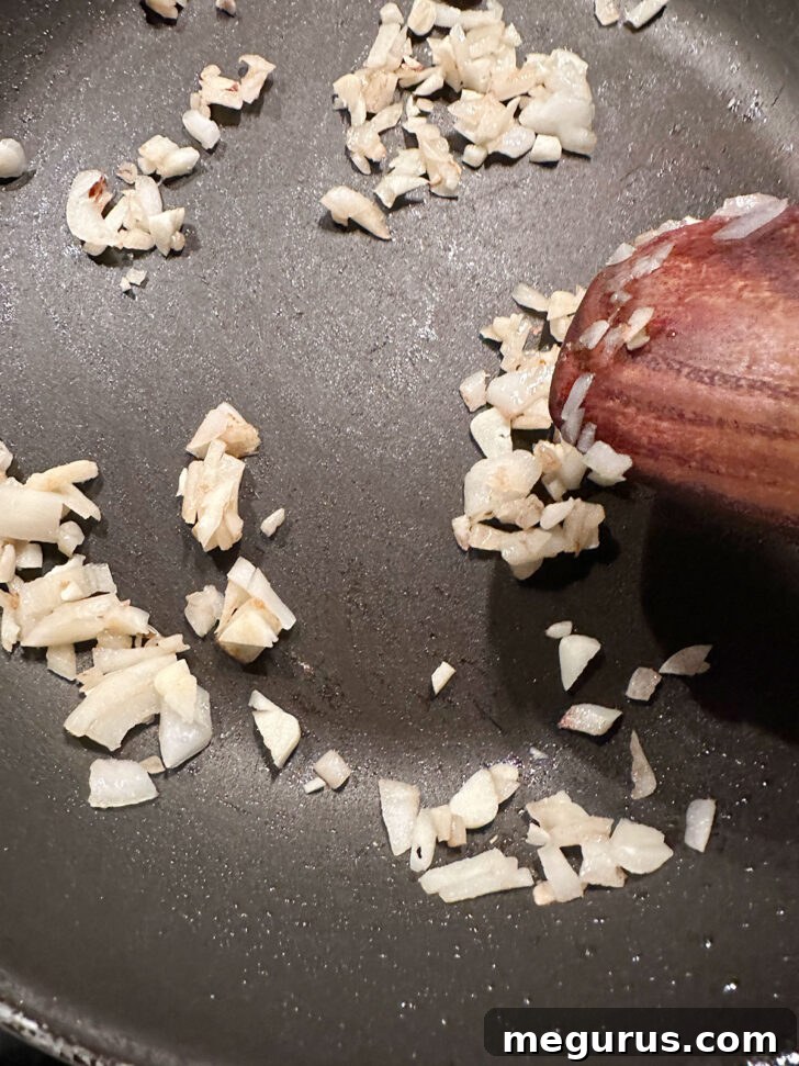 Diced onions cooking in a skillet with a bit of oil, softening and becoming translucent.