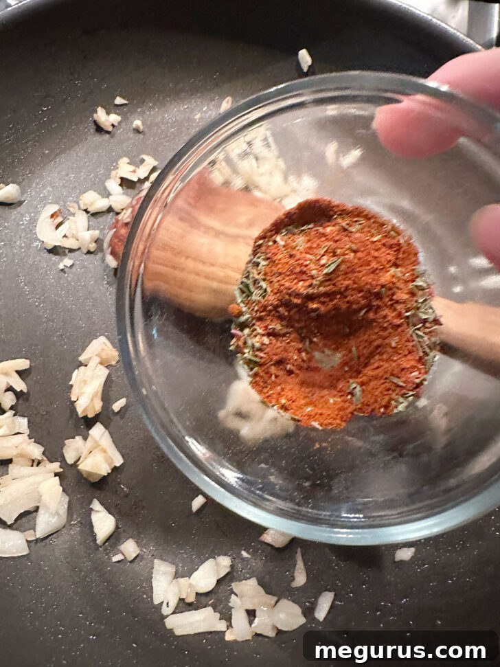 A vibrant mix of Cajun spices being added to the sautéed onions and garlic in the skillet.