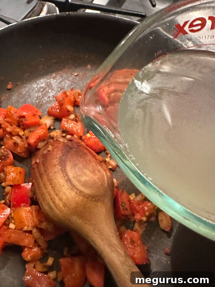 Chicken broth being poured into the skillet, deglazing the pan and forming the sauce base.