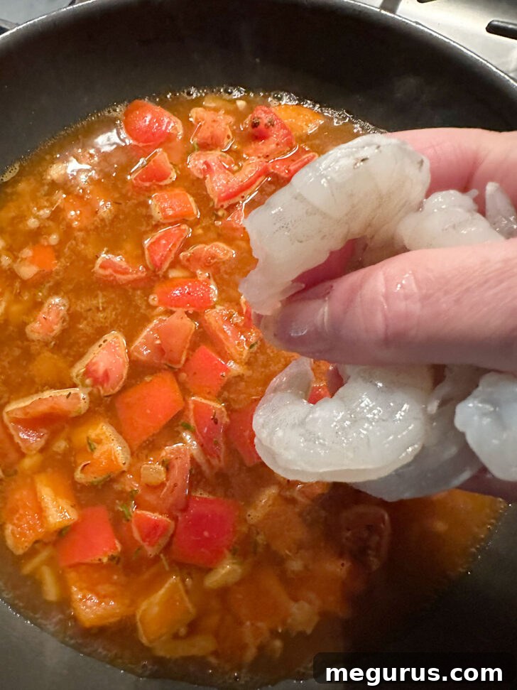 Raw shrimp scattered into the simmering Cajun sauce in the skillet, ready to cook.