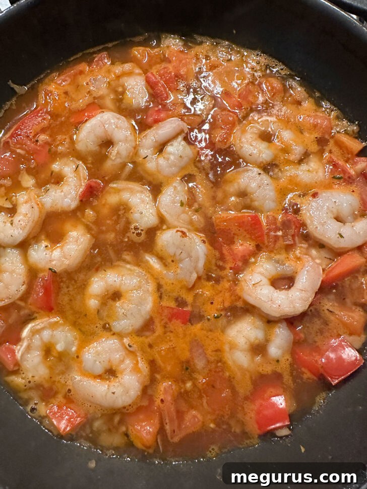 Perfectly cooked shrimp simmering in the rich, red Cajun sauce, showing its opaque pink color.