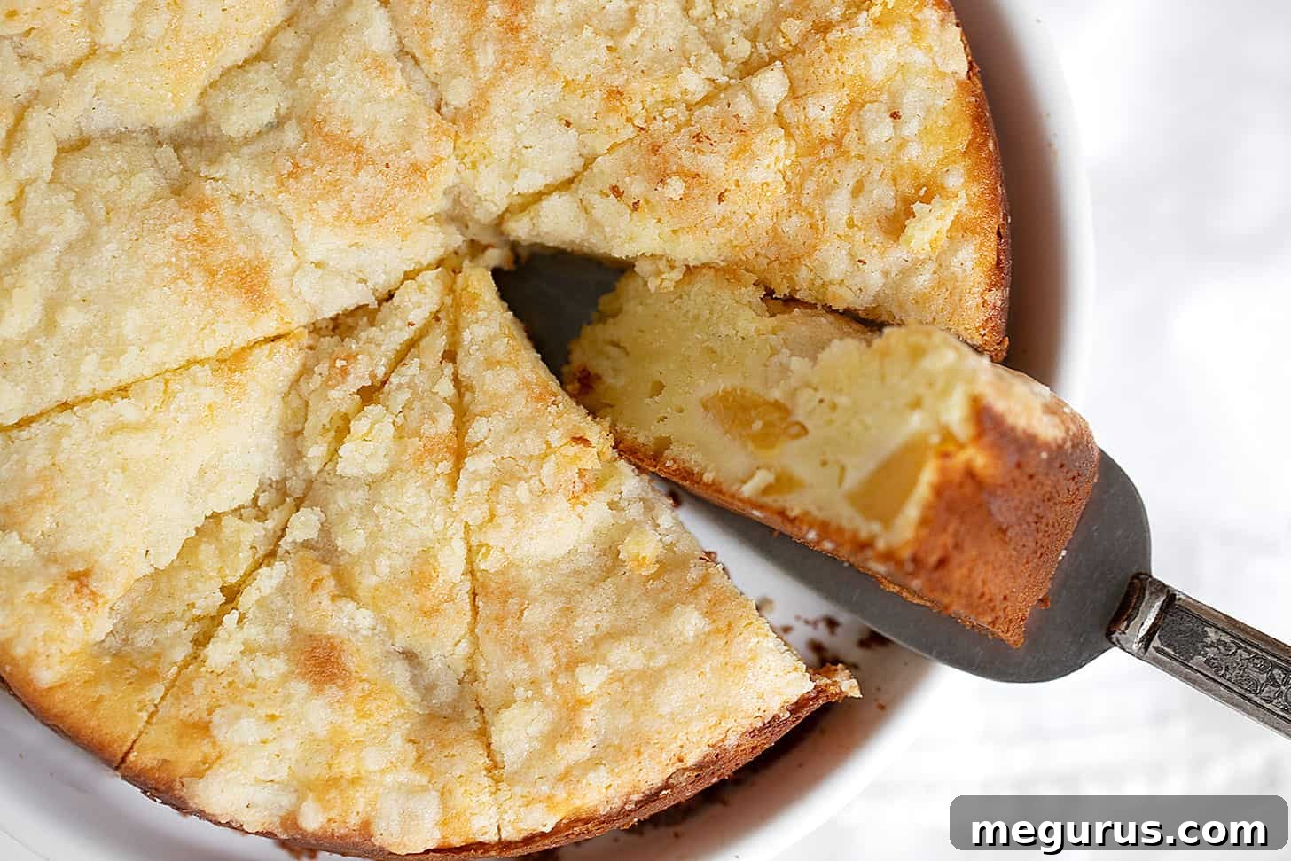 A generous slice of Peach Cream Cheese Cake, showcasing its tender crumb, luscious peach pieces, and delicate crumb topping, served on a pristine white plate.