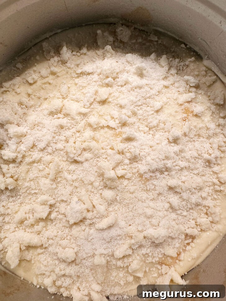 The peach cream cheese cake batter spread evenly in a baking pan, topped generously with crumb mixture, ready for the oven.