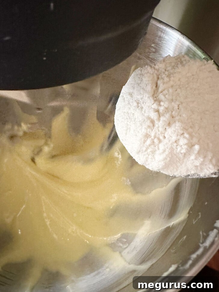 A portion of the flour mixture being added to the wet ingredients in the mixing bowl, signifying the start of alternating dry and wet additions.