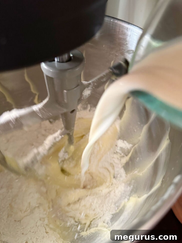 A stream of milk being poured into the mixing bowl, alternating with the dry ingredients for a perfectly blended cake batter.