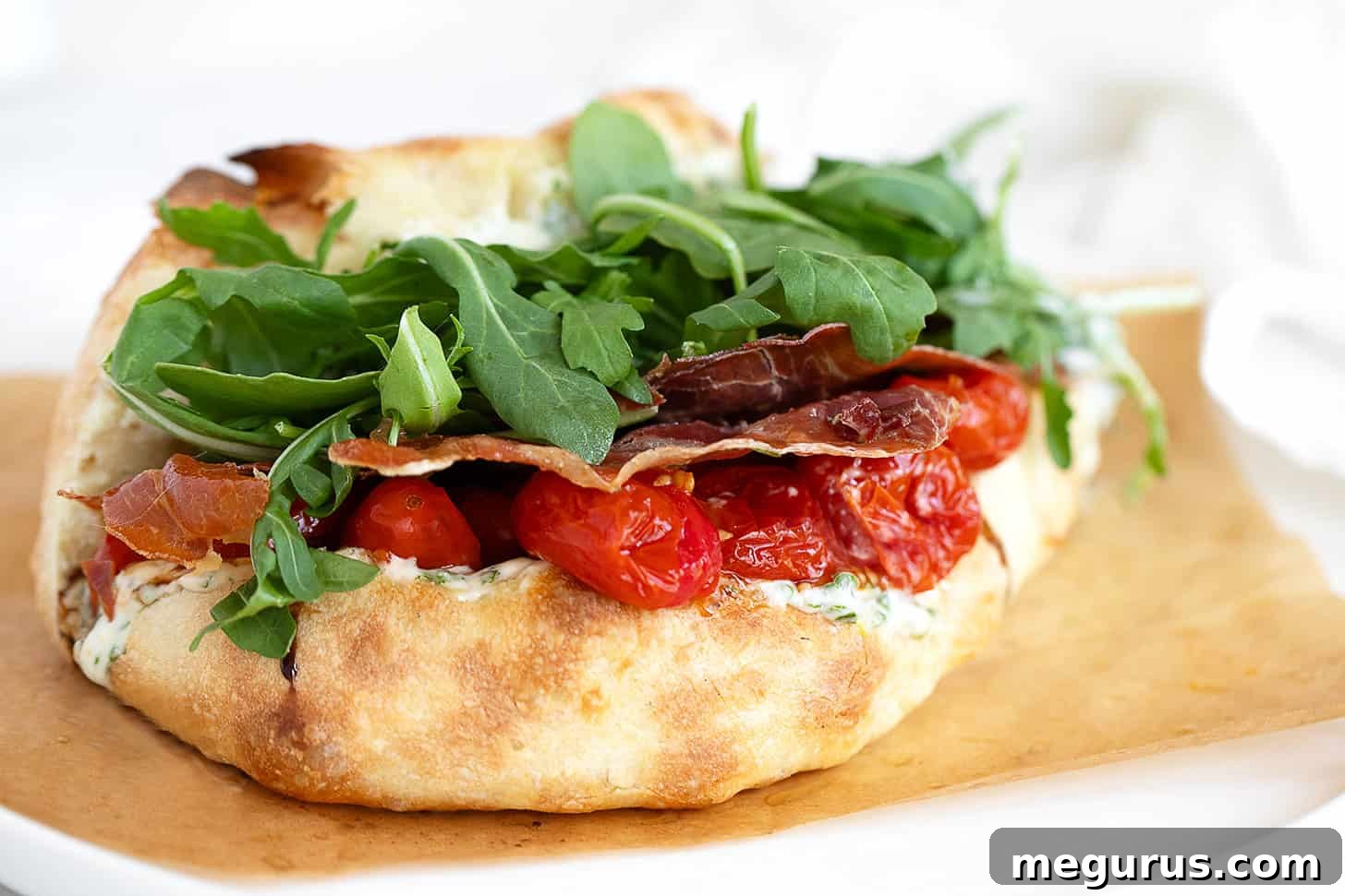 A delicious BLT pizza sandwich on parchment paper, showcasing its rich ingredients and golden crust.