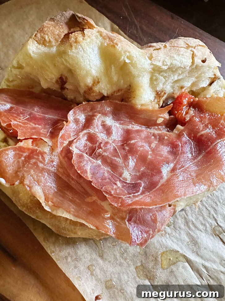 Crispy prosciutto slices arranged on top of the roasted tomatoes within the pizza sandwich.