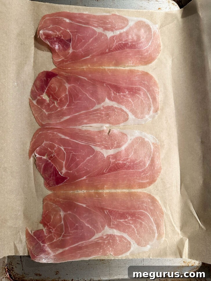 Thin slices of prosciutto arranged on a parchment-lined baking sheet, ready for baking.