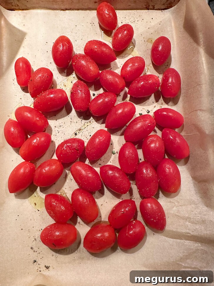 Vibrant cherry tomatoes scattered on a parchment-lined baking sheet, drizzled with olive oil.