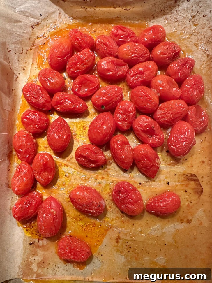 Roasted cherry tomatoes, softened and slightly caramelized, on a baking sheet.