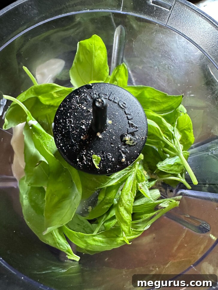 Ingredients for basil mayo, including fresh basil leaves and mayonnaise, in a food processor.