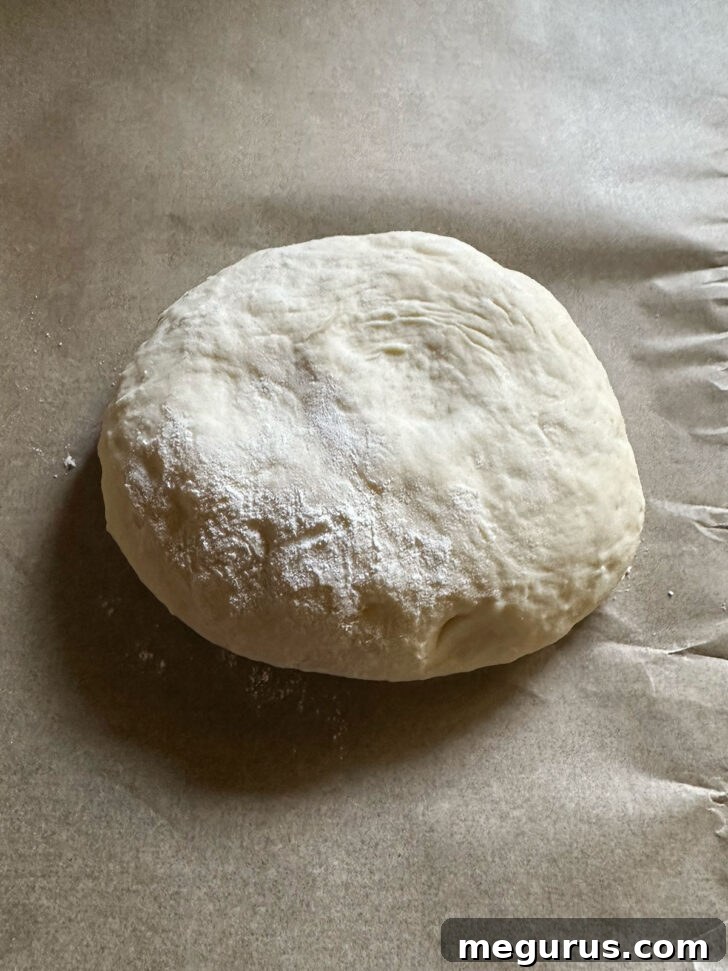 A portion of pizza dough resting on parchment paper, dusted with flour.