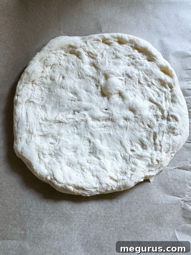 Pizza dough pressed into a neat circular shape on parchment paper.